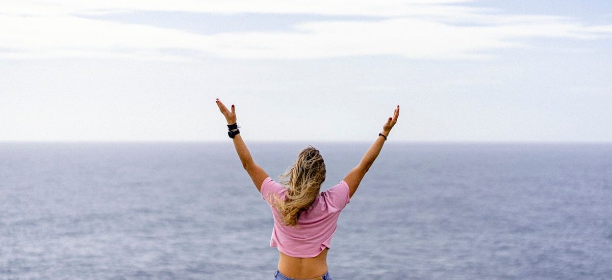 a woman with her arms raised in front of a body of water