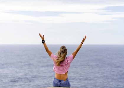 a woman with her arms raised in front of a body of water