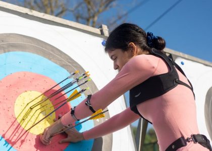 A female archer adjusts arrows on a target during a sunny day, showcasing precise archery skills.
